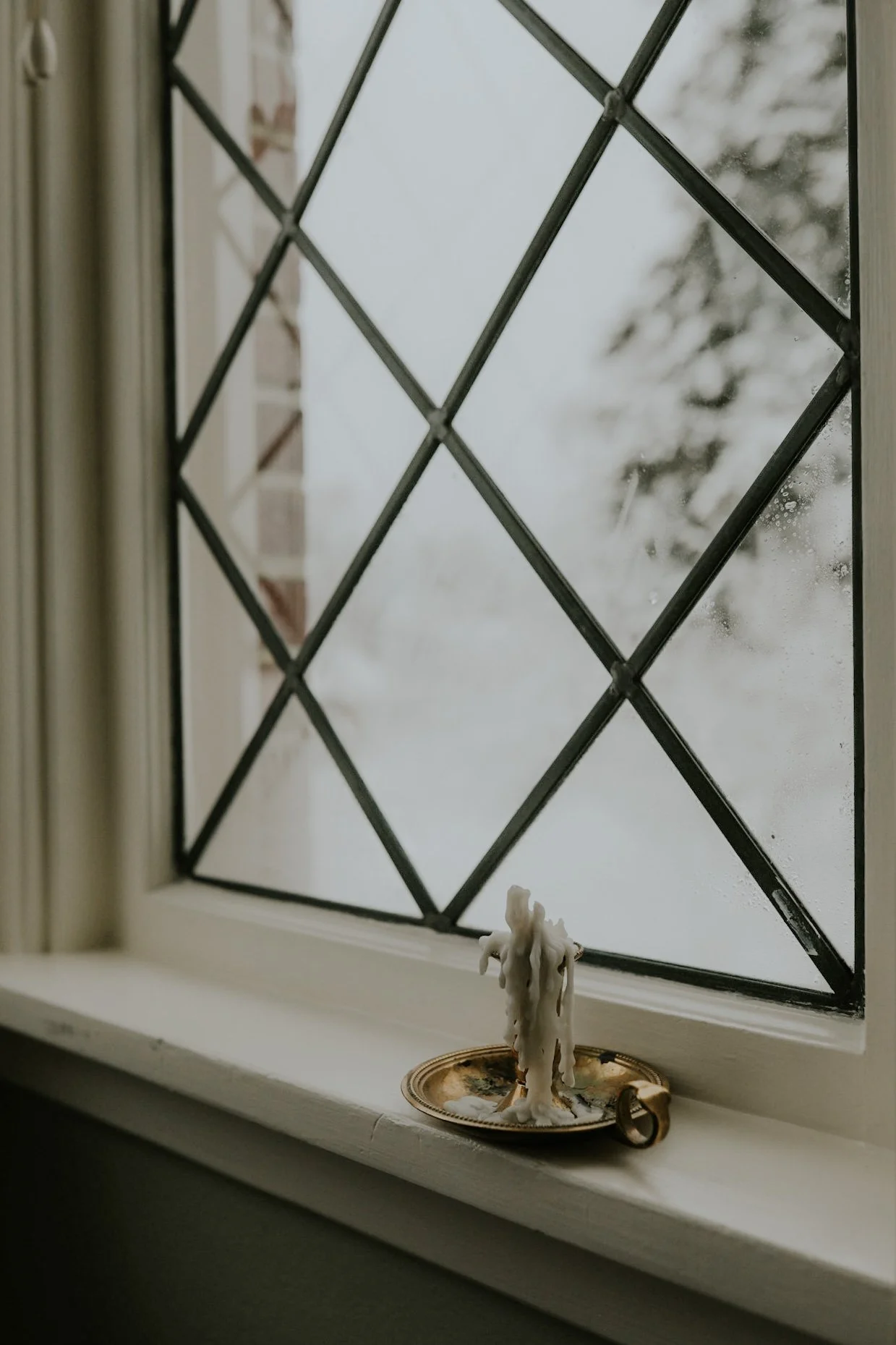 Melted candle on brass holder by lattice window
