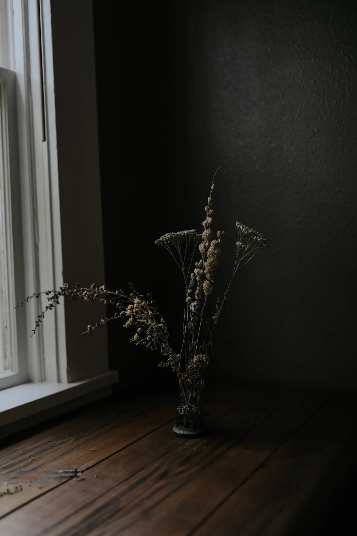 Dried flowers in a vase on a wooden table near a window in dim lighting.