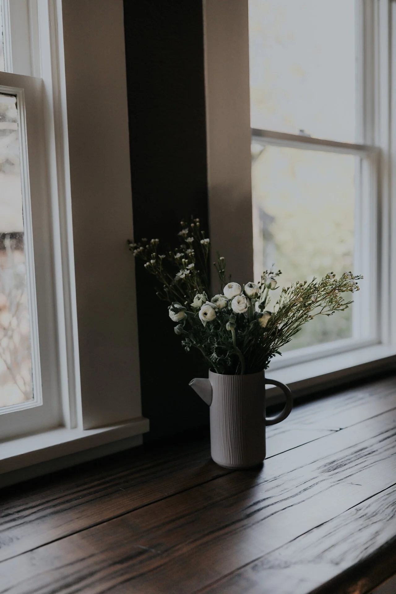 White flowers in ceramic pitcher on wooden table by window
