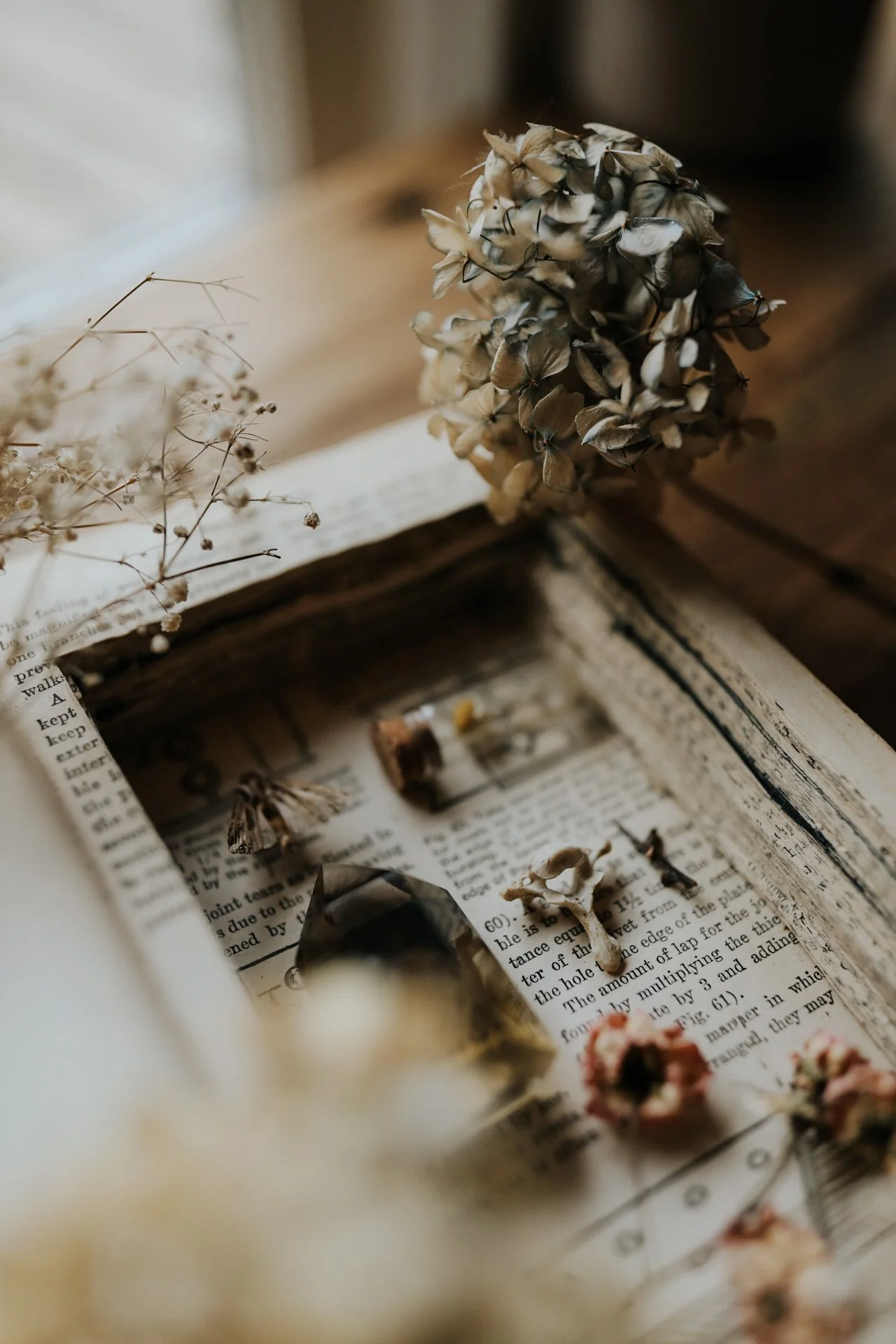 Vintage collage with dried flowers, open book, delicate glass vial, and prism on wooden surface.