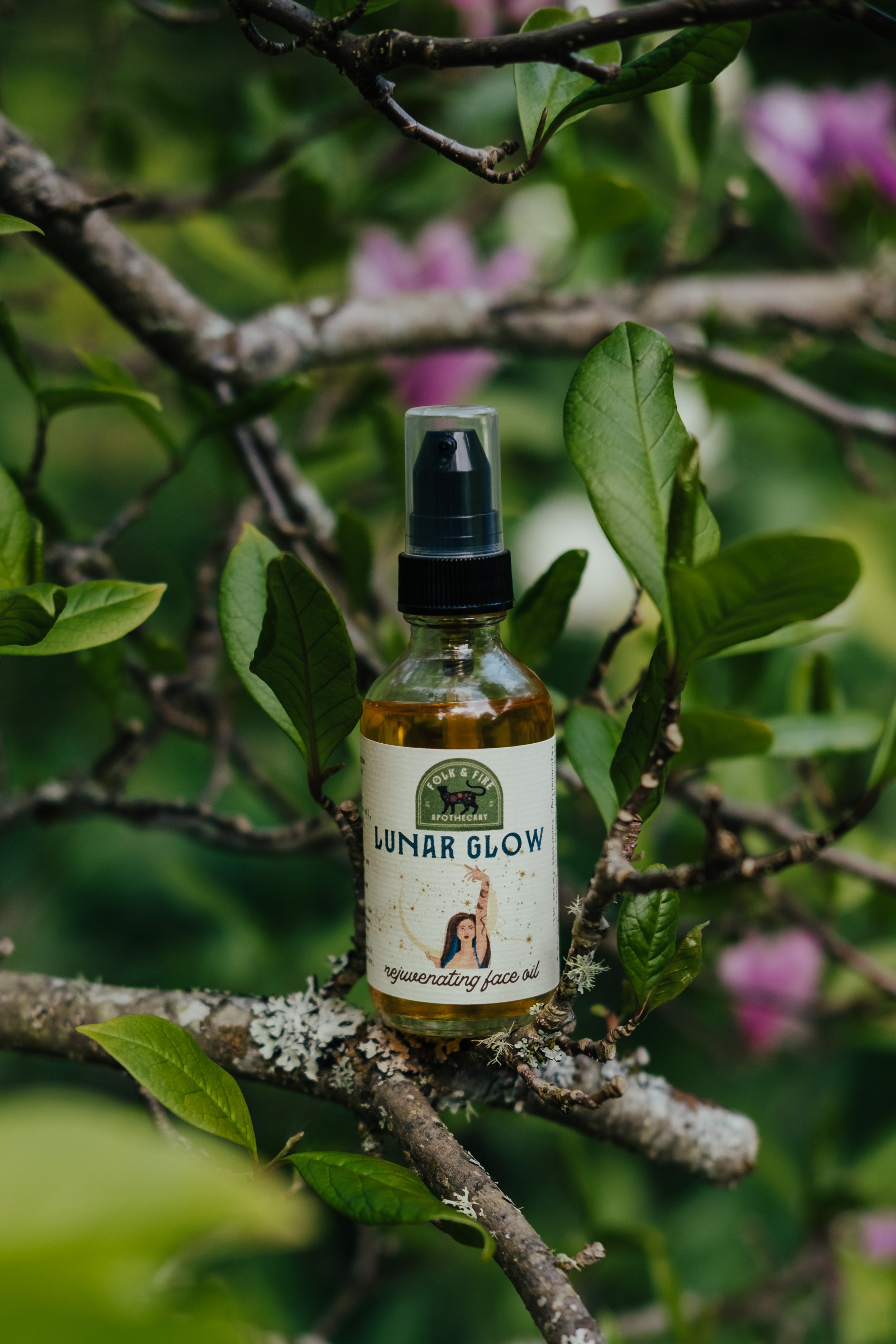 Lunar Glow face oil bottle on a tree branch with green leaves background.