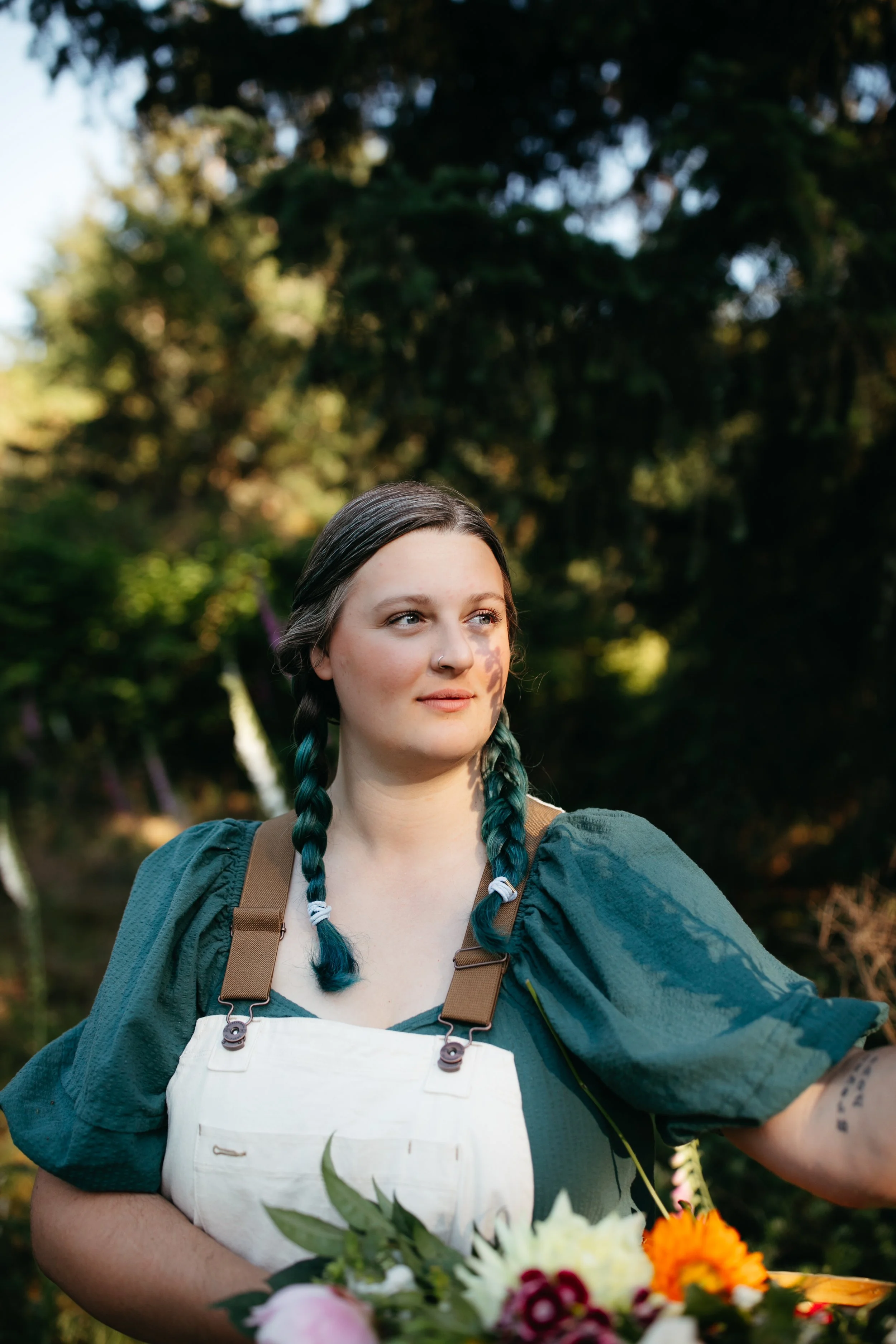 Woman with teal braids holding a bouquet of flowers in a garden.