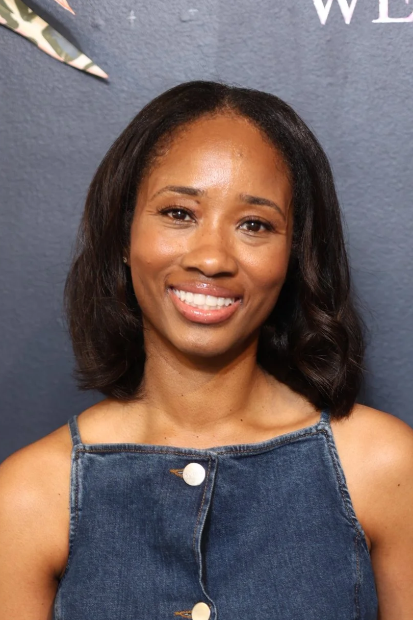 Close-up of a smiling woman with black hair, in an indoor setting with a blurred background.