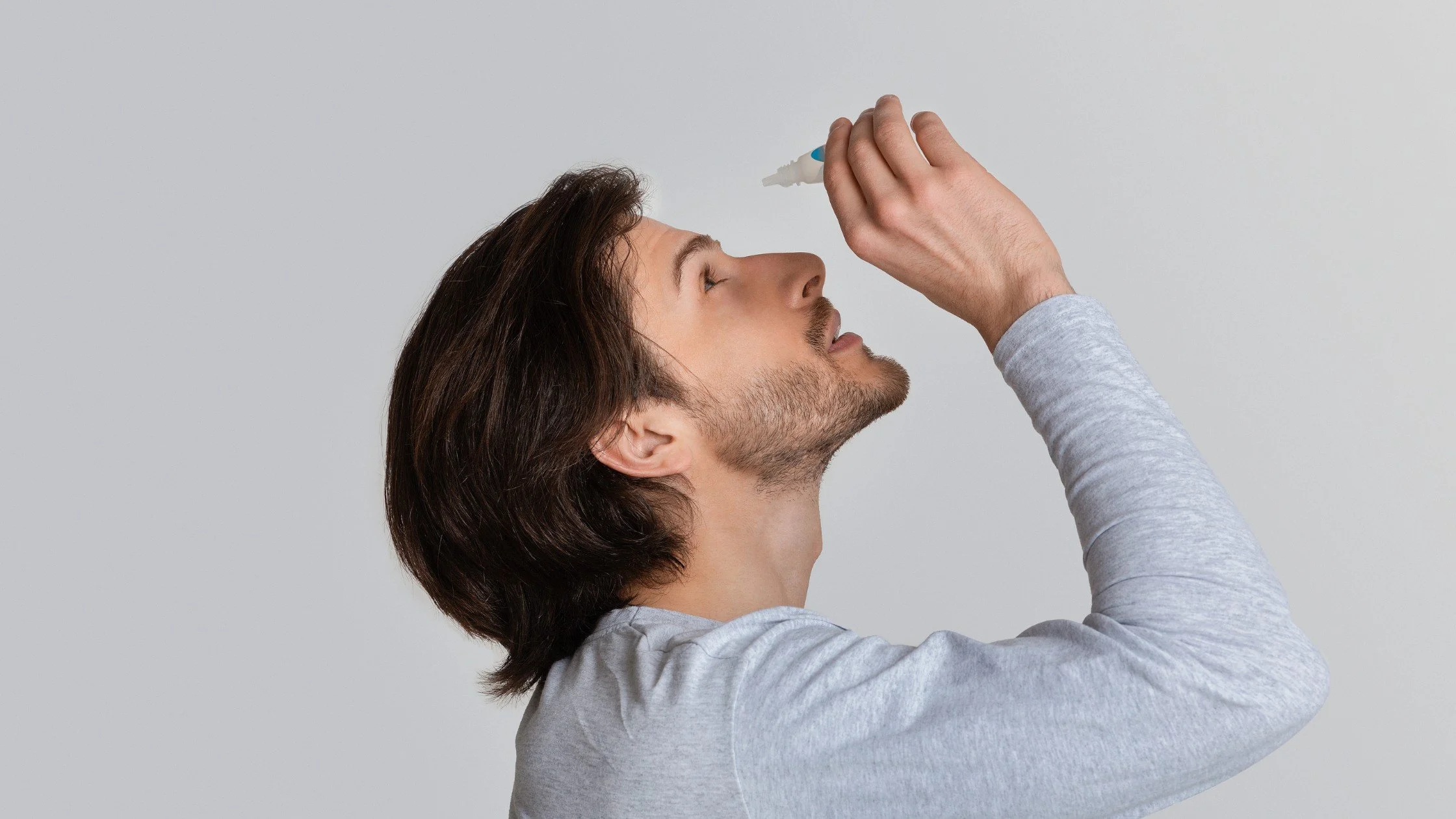 A man with dry eye putting eye drops in his eyes.