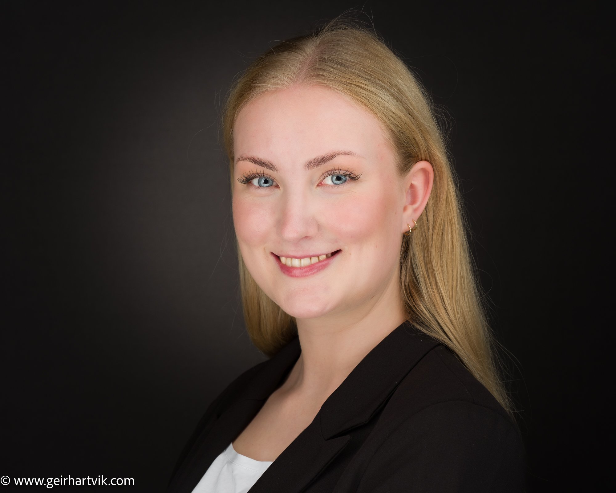 Portrett av en smilende kvinne med blondt hår mot en svart bakgrunn.