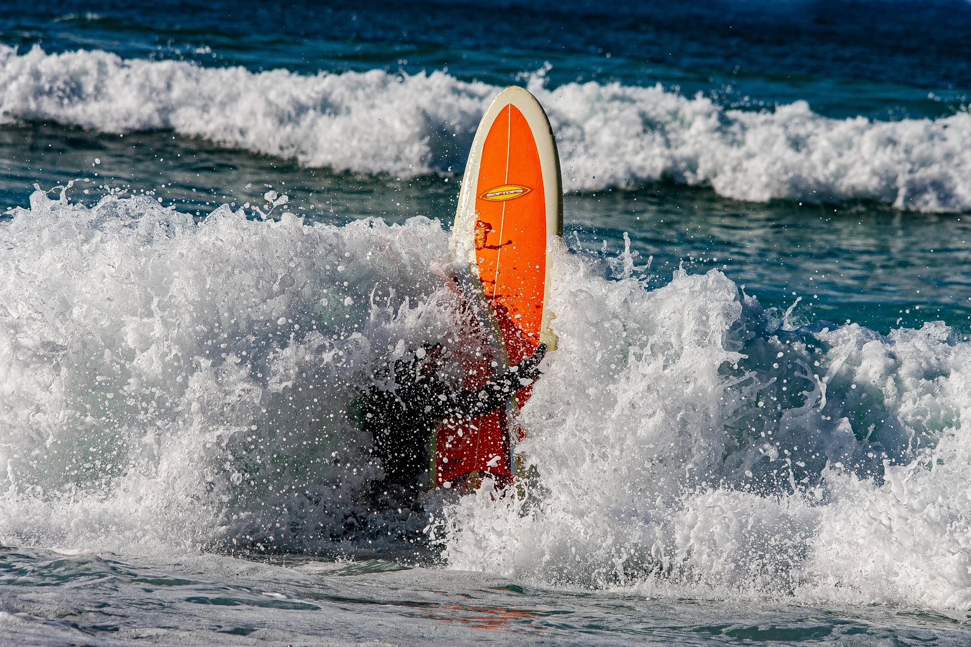 En person på en surfebrett i havet, dekket av bølger.