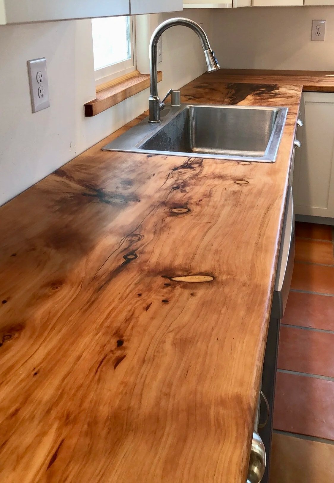 Modern kitchen with wooden countertop, stainless steel sink, tall faucet, and white cabinets with glass doors.