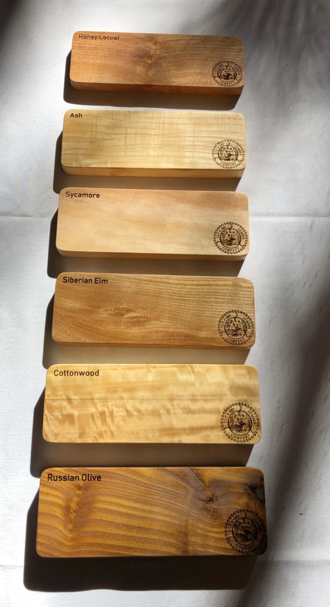 Wood samples labeled as Honey Locust, Ash, Sycamore, Siberian Elm, Cottonwood, and Russian Olive, with branded logos in the corners.
