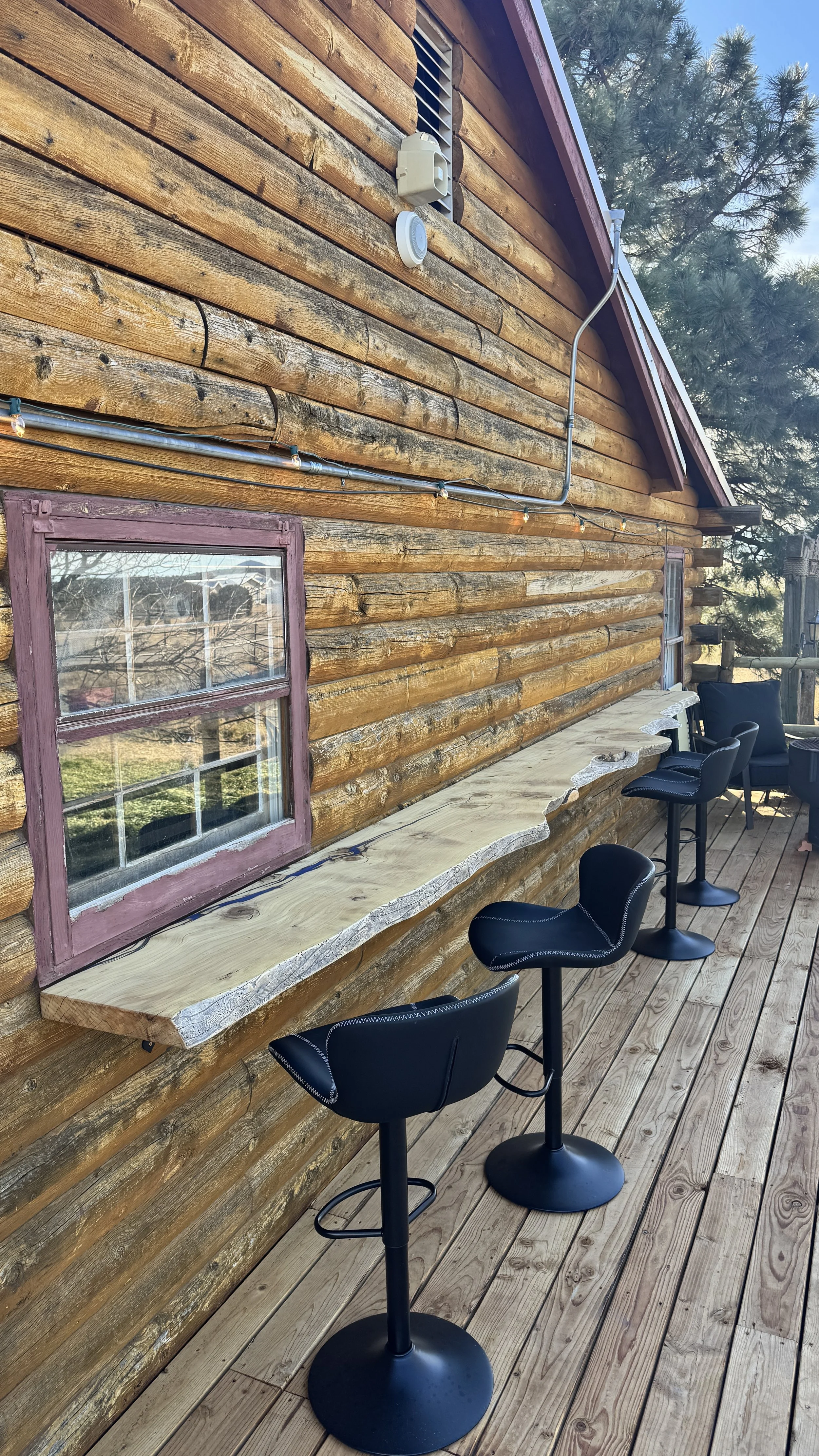 Long wood live-edge bar top mounted on the side of a log cabin in the mountains.