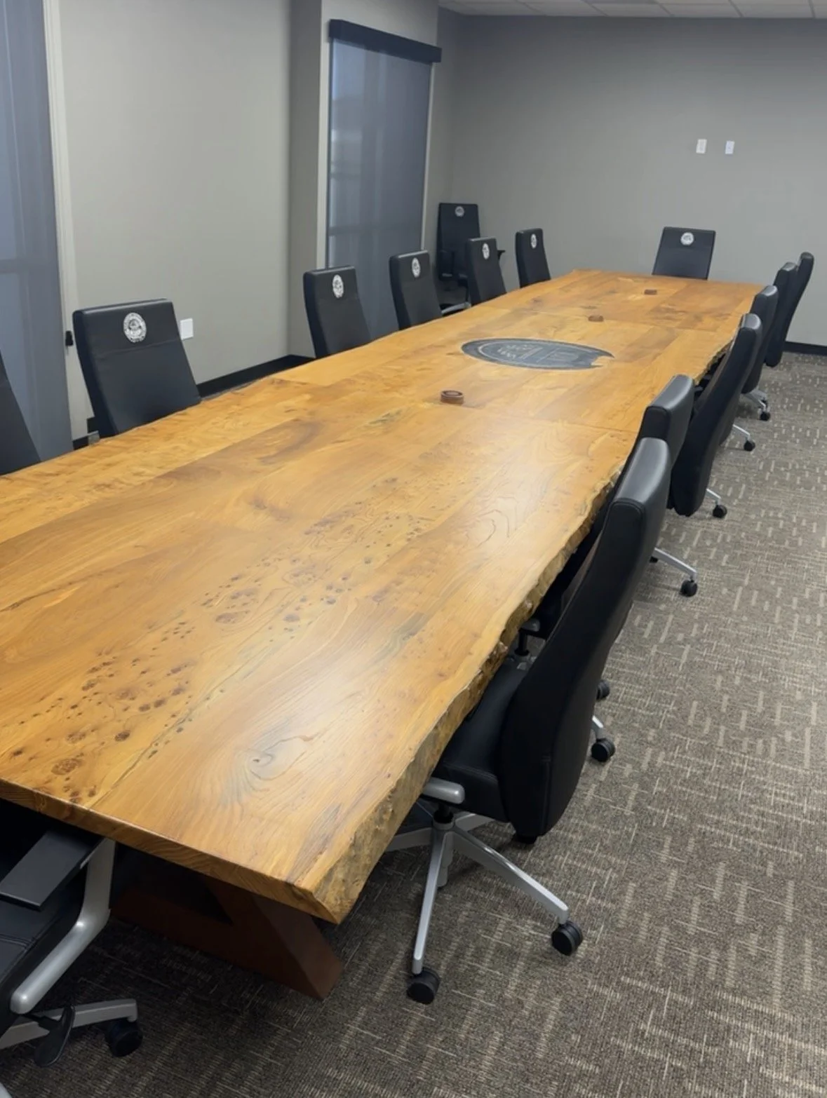 Large wood conference table with a metal logo inlay in a business meeting room with several chairs.