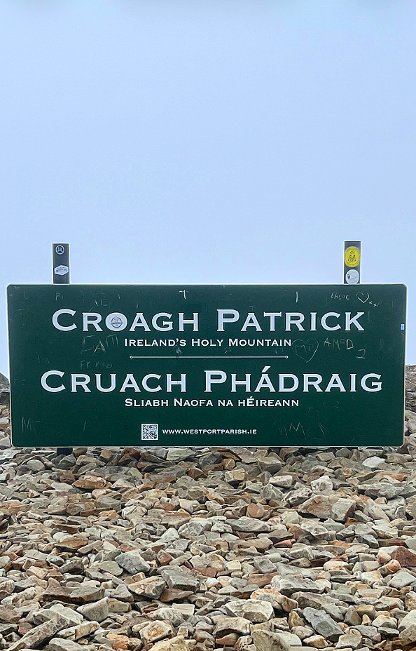 A green summit sign that reads "CRUACH PHÁDRAIG, SLIABH NAOFA NA HÉIREANNCroagh Patrick, Ireland’s Holy Mountain"