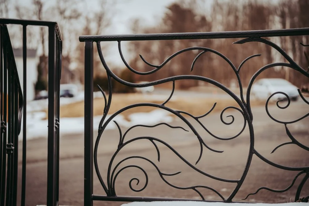 Black wrought iron railing with swirling scroll panels in front of a snowy yard