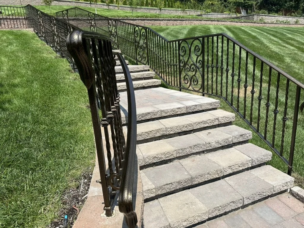 Curved wrought iron style handrail along natural stone steps cut into a lawn