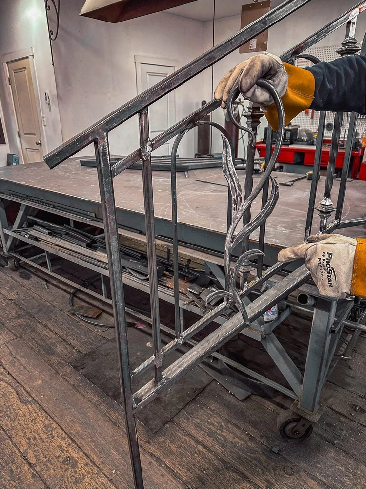 Fabricator fitting a hand-formed scroll panel into a railing section at The Iron Shop