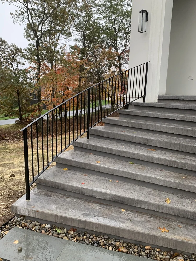 Black metal railing with vertical pickets beside wide stone front entry steps