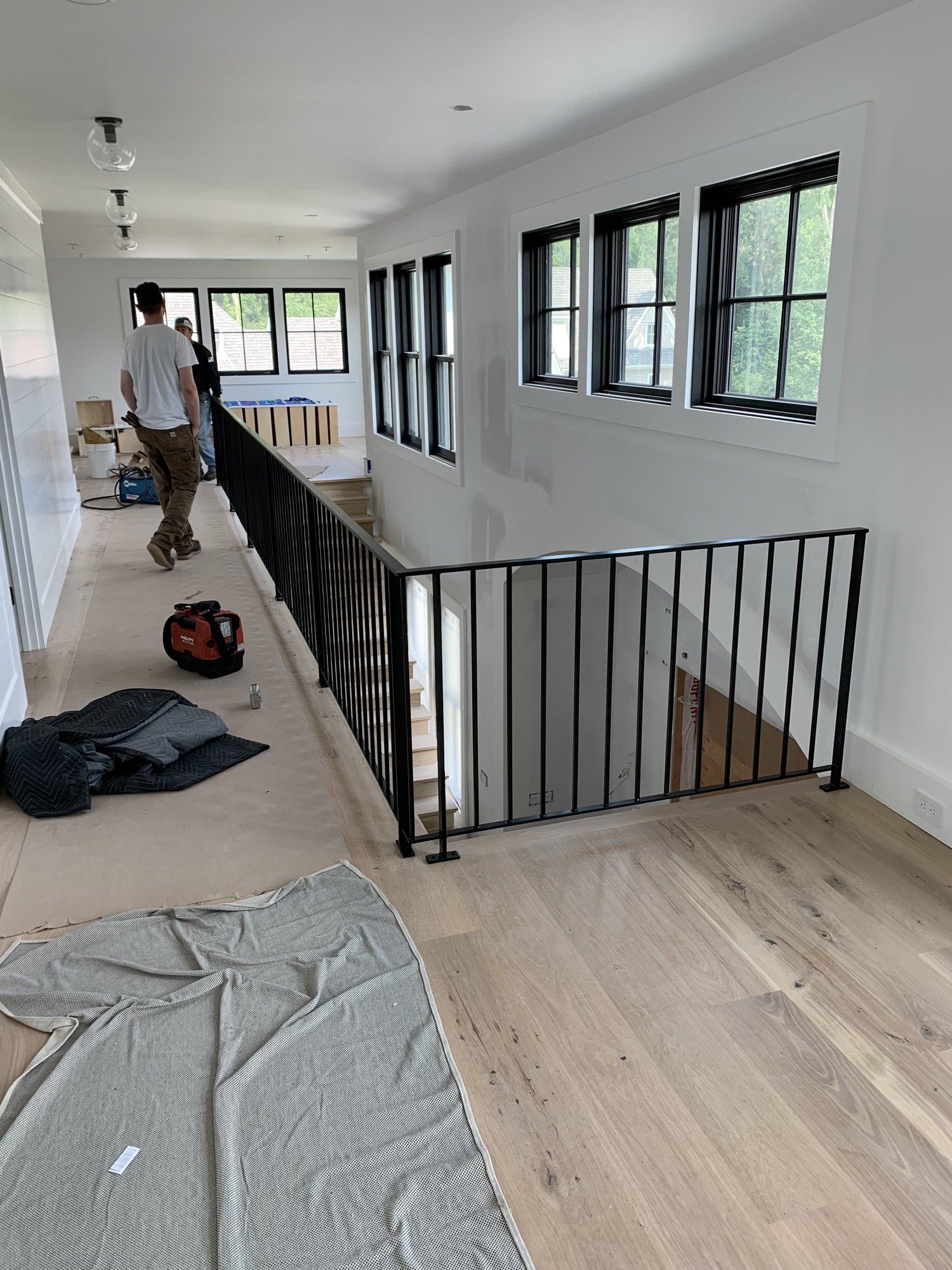 Upper hallway railing with black pickets being installed over a wood floor