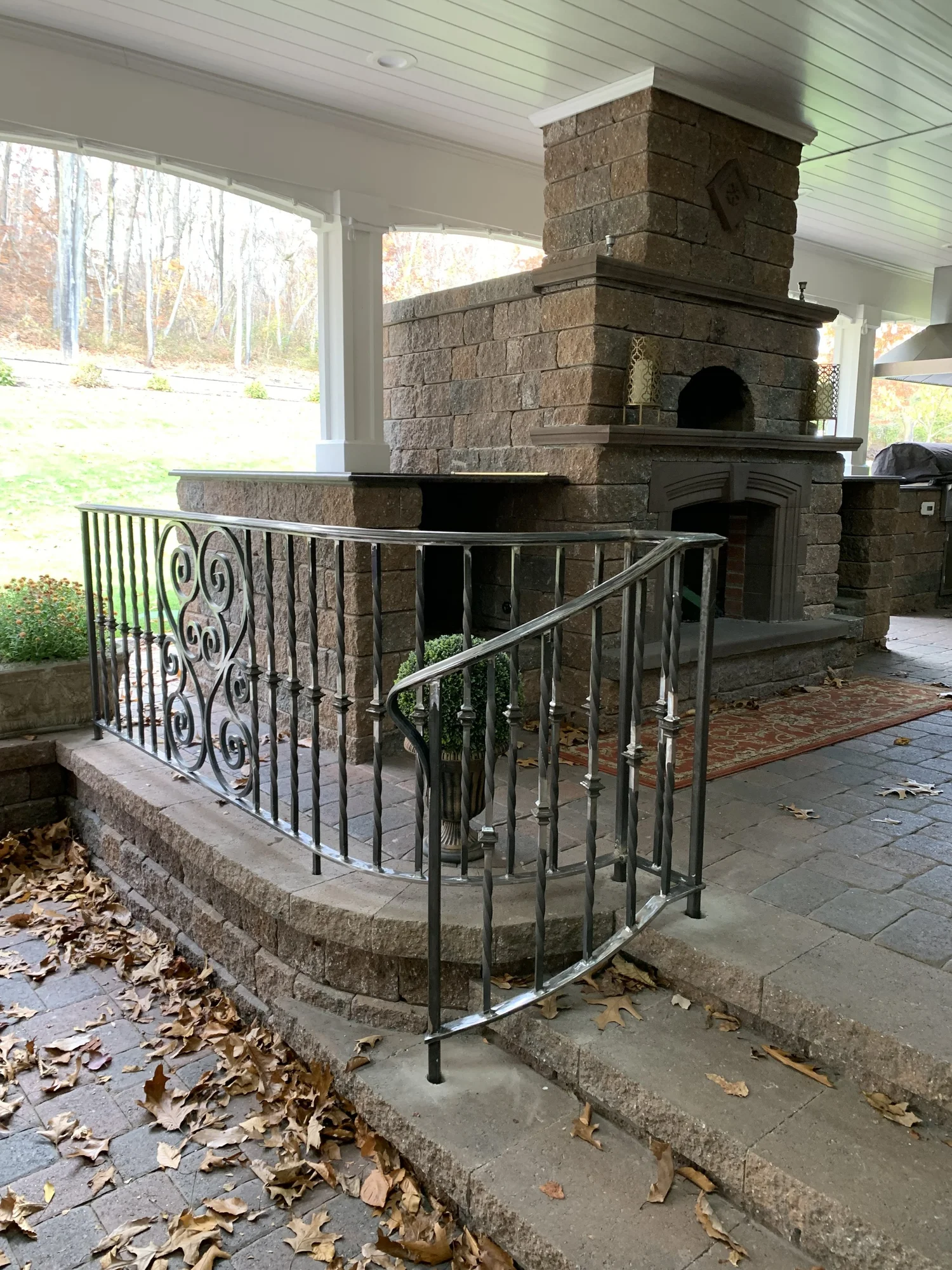 Curved iron railing around a stone patio with an outdoor fireplace