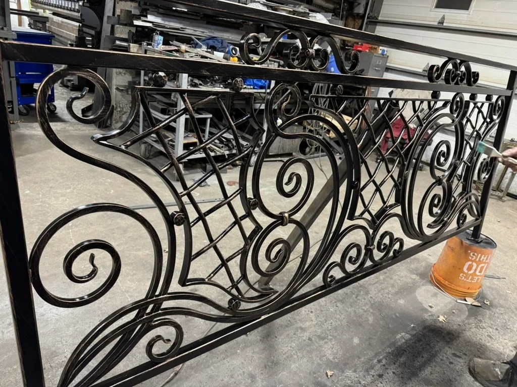 Black scrollwork railing section on the floor of the Iron Shop fabrication shop