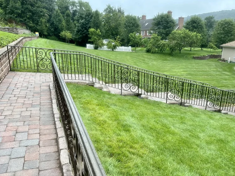 Black wrought iron railing with scroll panels along a paver walkway above a lawn