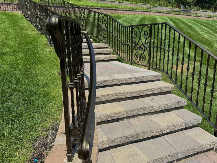 Curved black wrought iron handrail beside stone garden steps
