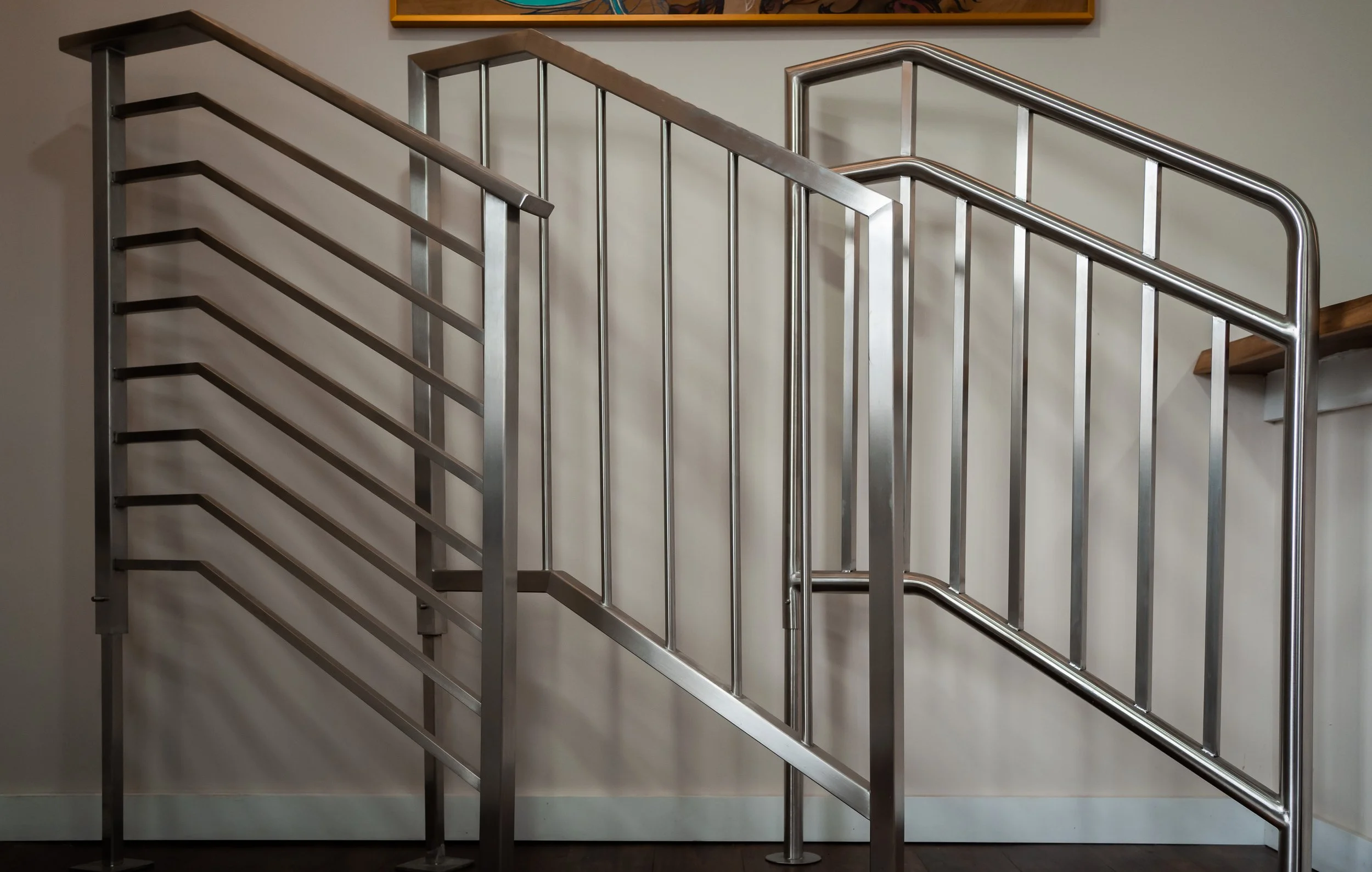 Stainless steel indoor staircase with handrails and vertical balusters, mounted against a plain wall.