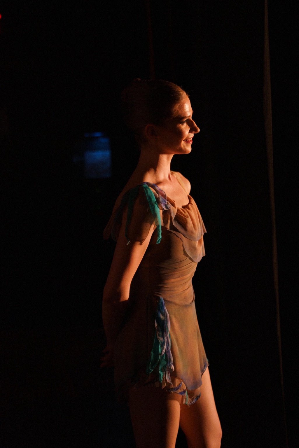 A dancer in warm stage light against a dark background.