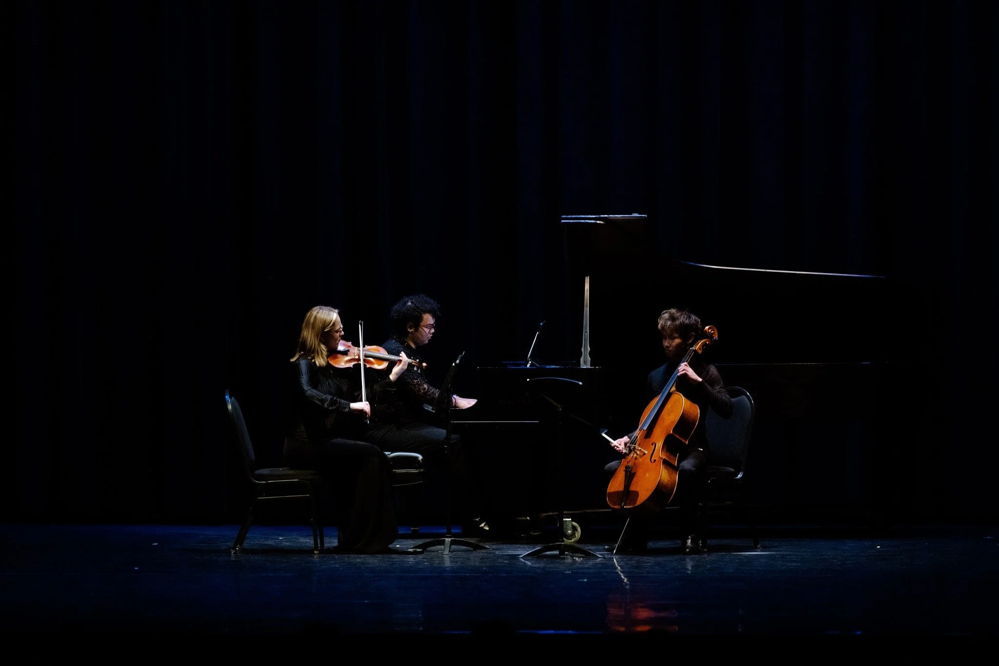 Violin, piano and cello musicians performing together on stage.