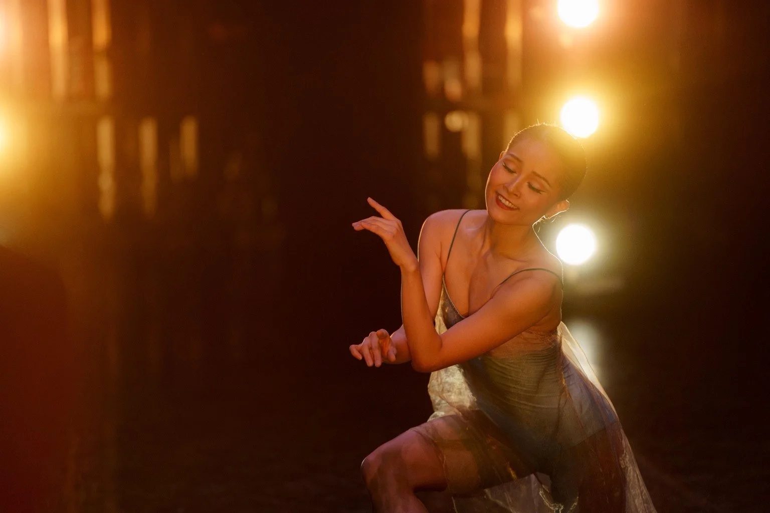 A dancer in a flowing teal costume, illuminated by golden stage lights.