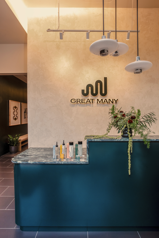 Great Many Atlanta custom green reception desk with marble counter. Hanging pendants light the area and draw attention to the limewash wall and custom signage.