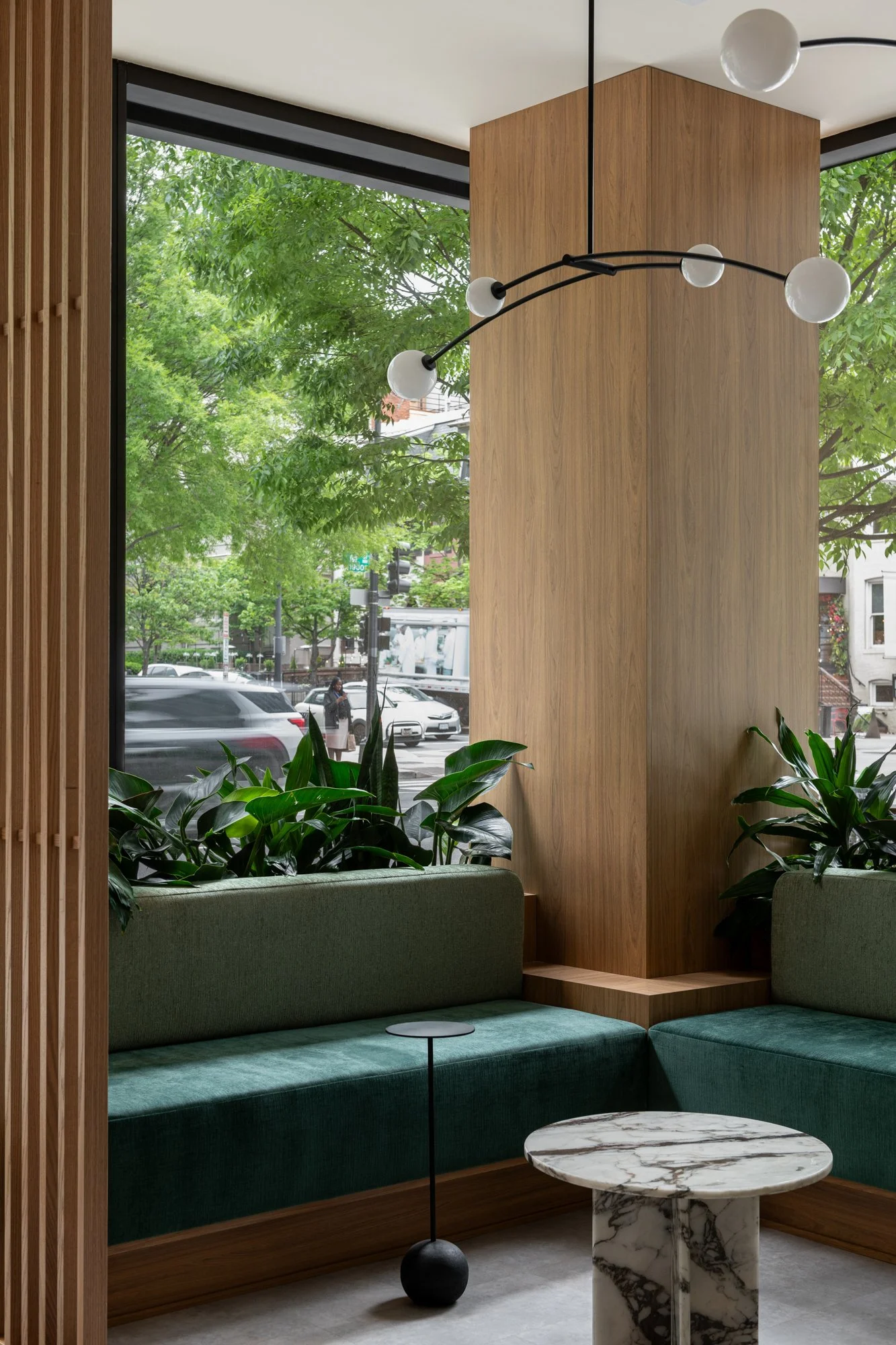 Waiting area in Great Many's Washington DC sutdio with two-tone green upholstery and warm wood accents, surrounded by greenery