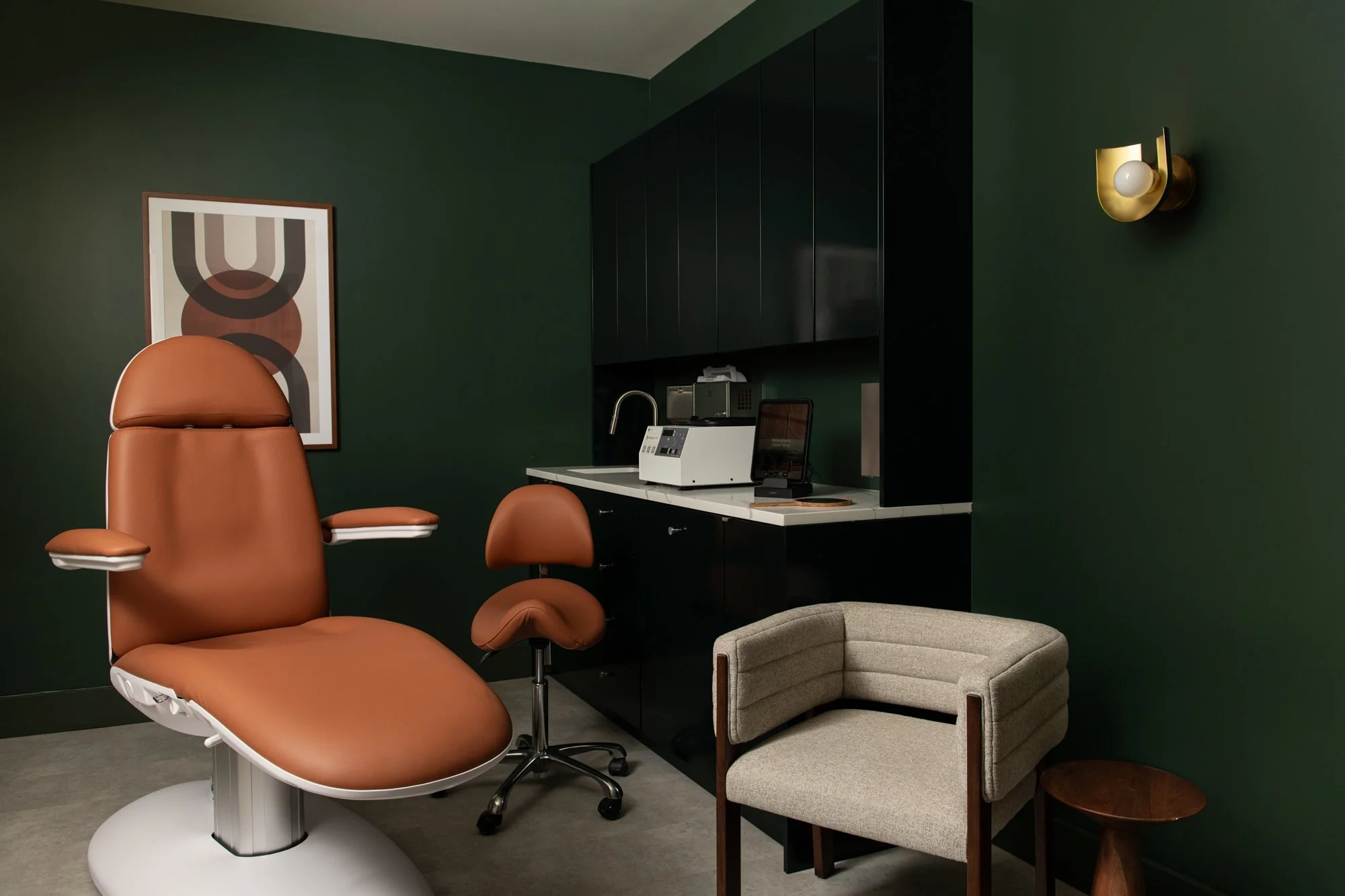 Treatment room at Great Many's Washington DC studio with a monochromatic green design, complemented by a warm camel leather chair
