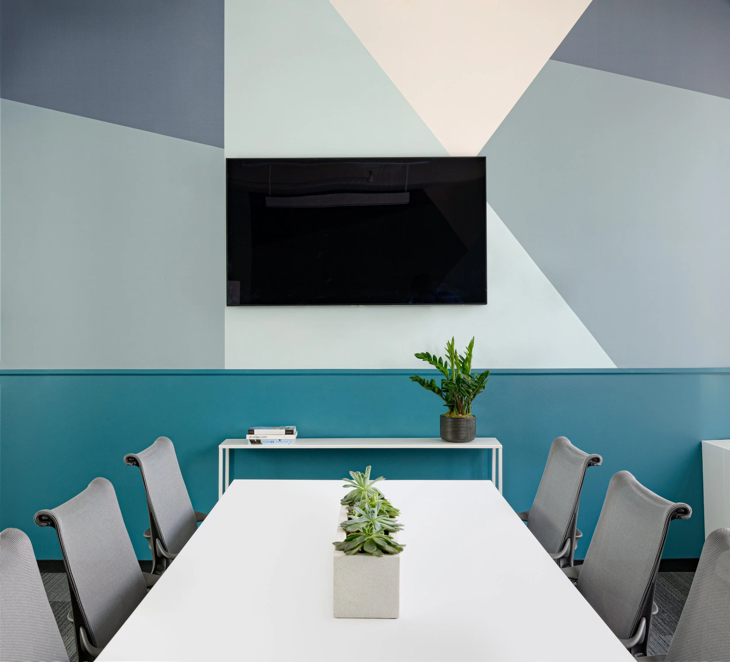 Conference room with blue abstract wallpaper, long white table, and gray desk chairs