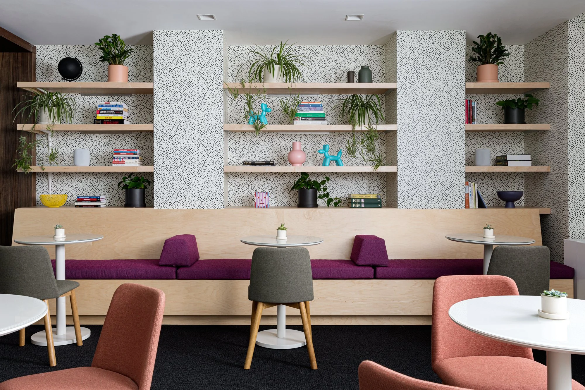 Seating area with banquettes, desk chairs, round tables, and white and black wallpaper