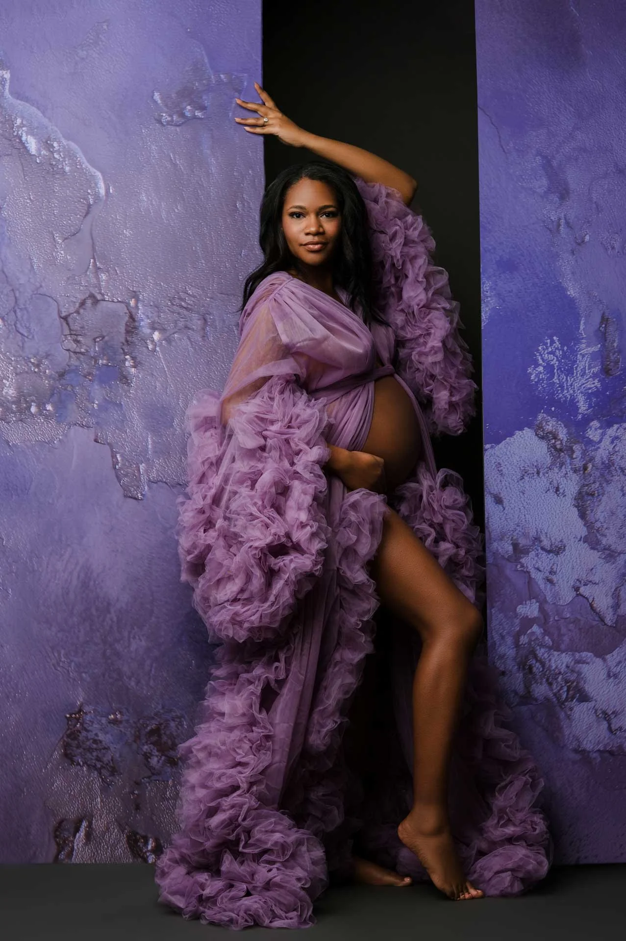 Pregnant woman in purple robe standing against purple wall in Seattle photography studio