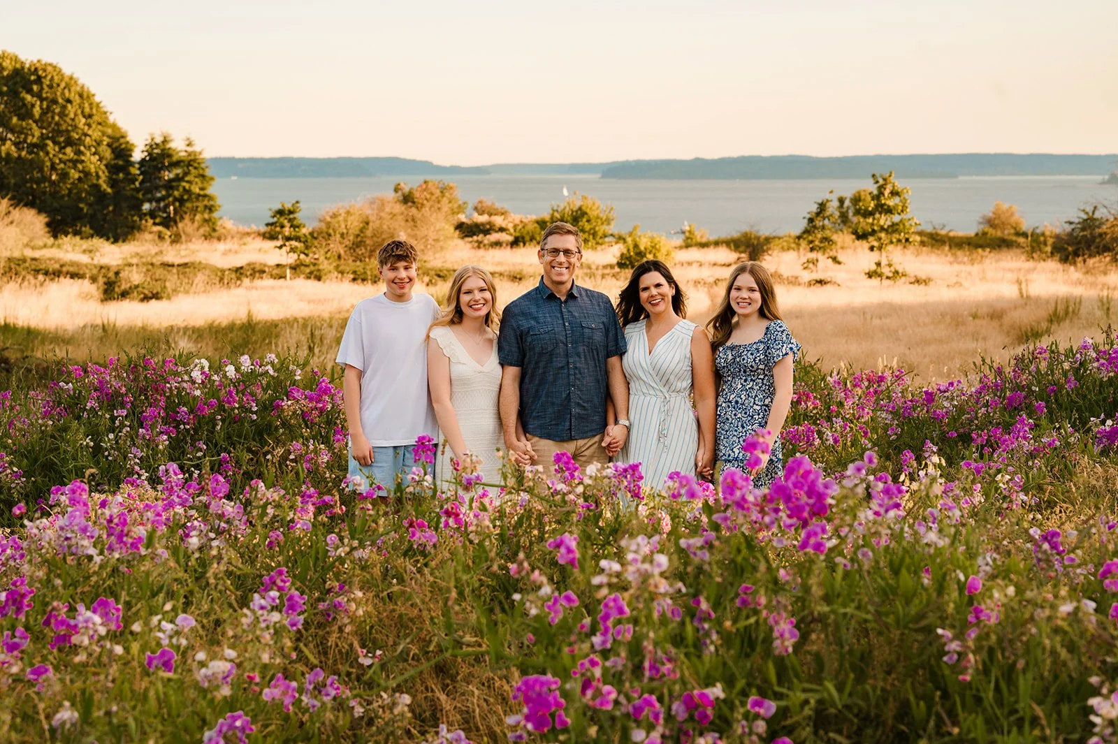 Best Seattle senior photos, family of 5 framed in a field of pink and white flowers with the ocean in the background behind them.