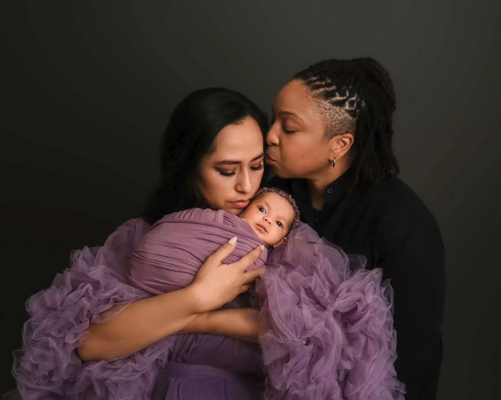 Two women holding their newborn baby in a studio newborn session