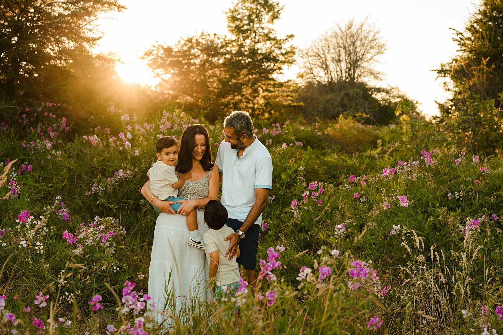 family of four surrounded by pink and white flowers and trees at golden hour sunshine