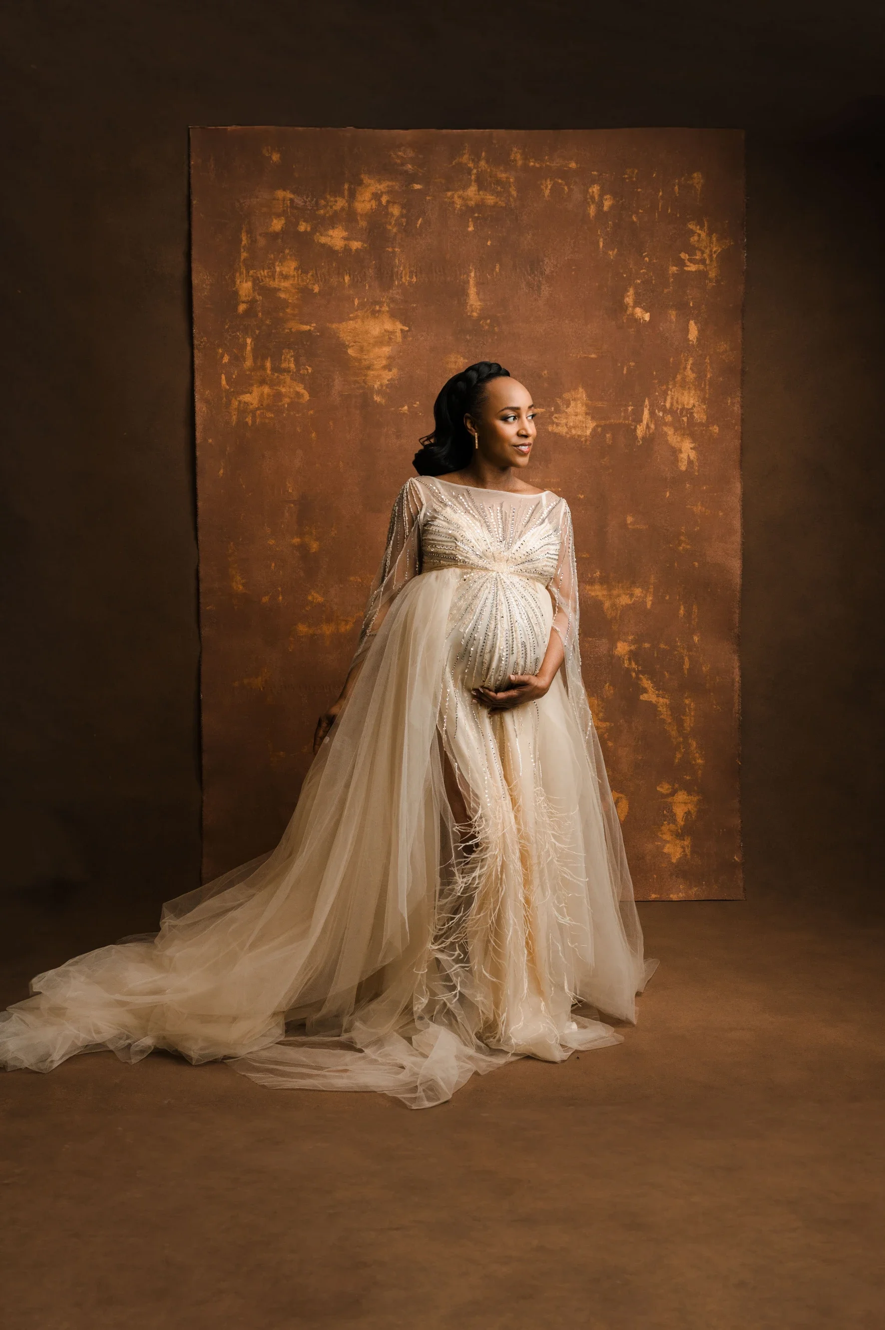 pregnant black woman in a sparkly tulle dress posed on brown canvas backdrop in studio
