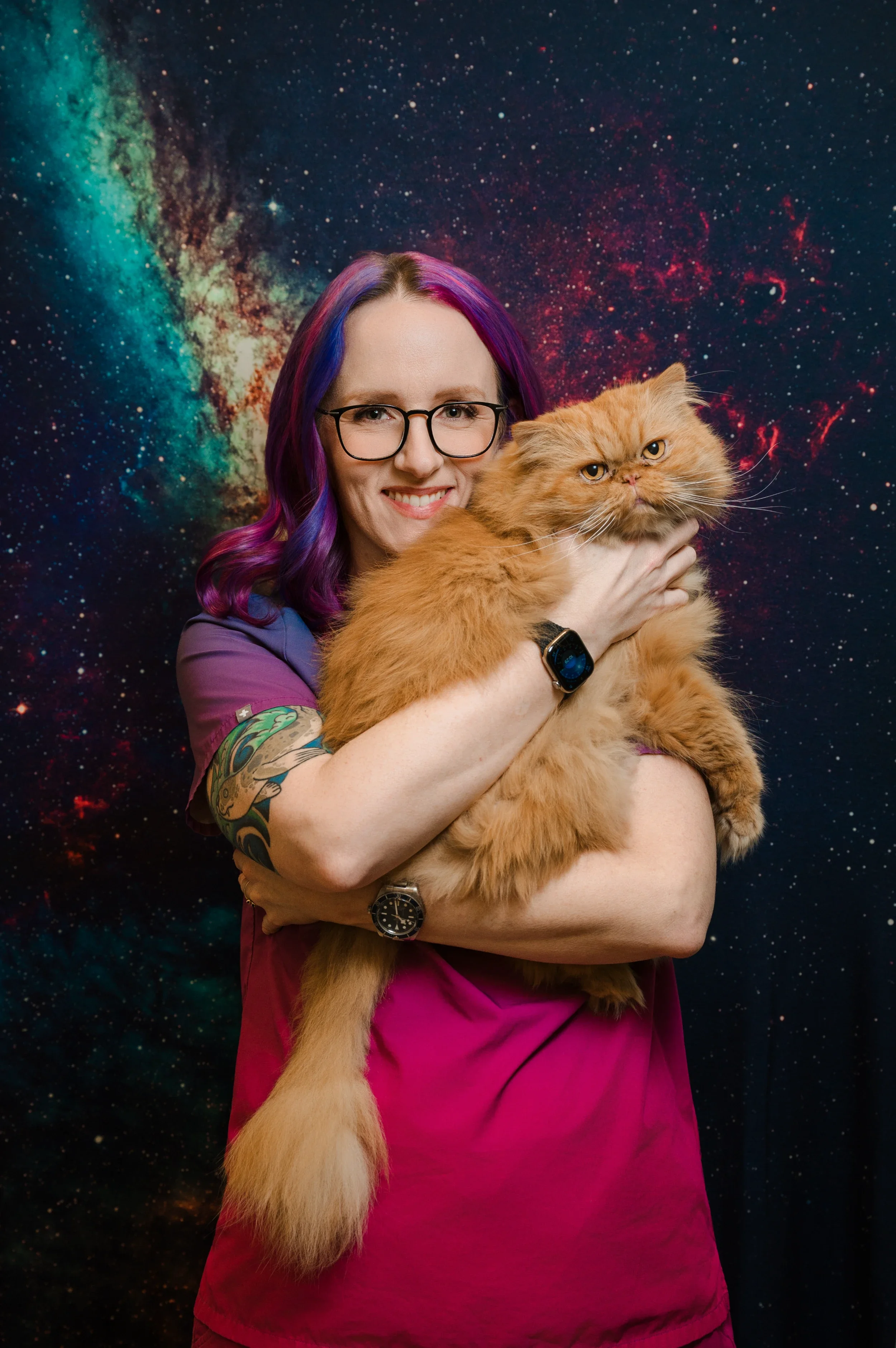 A woman with colorful purple and pink hair, wearing glasses and a purple and pink uniform, holding an orange Persian cat against a starry galaxy backdrop.