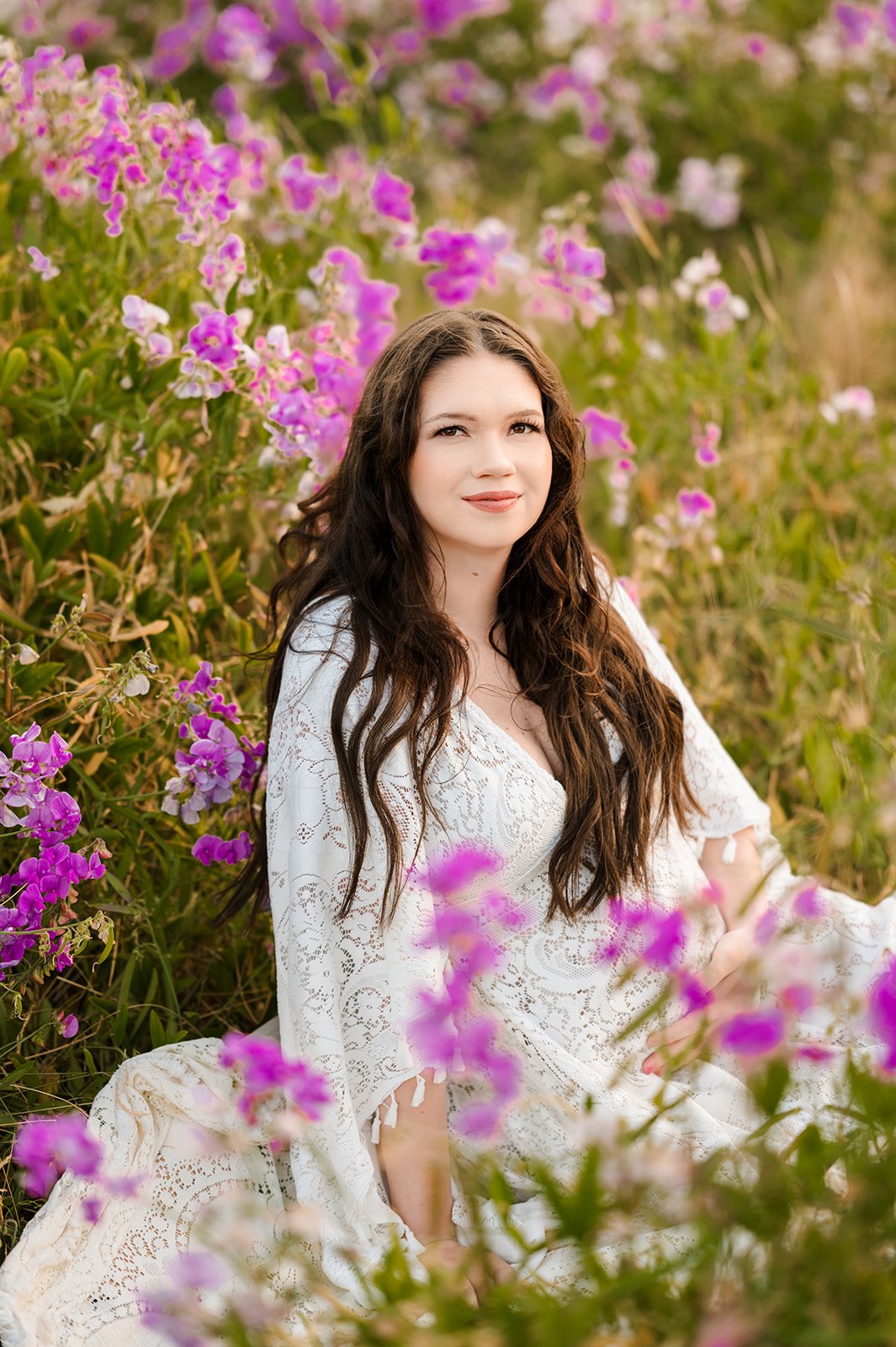 best maternity portraits Seattle showing a woman with brown hair sitting surrounded by pink and purple wildflowers in summer