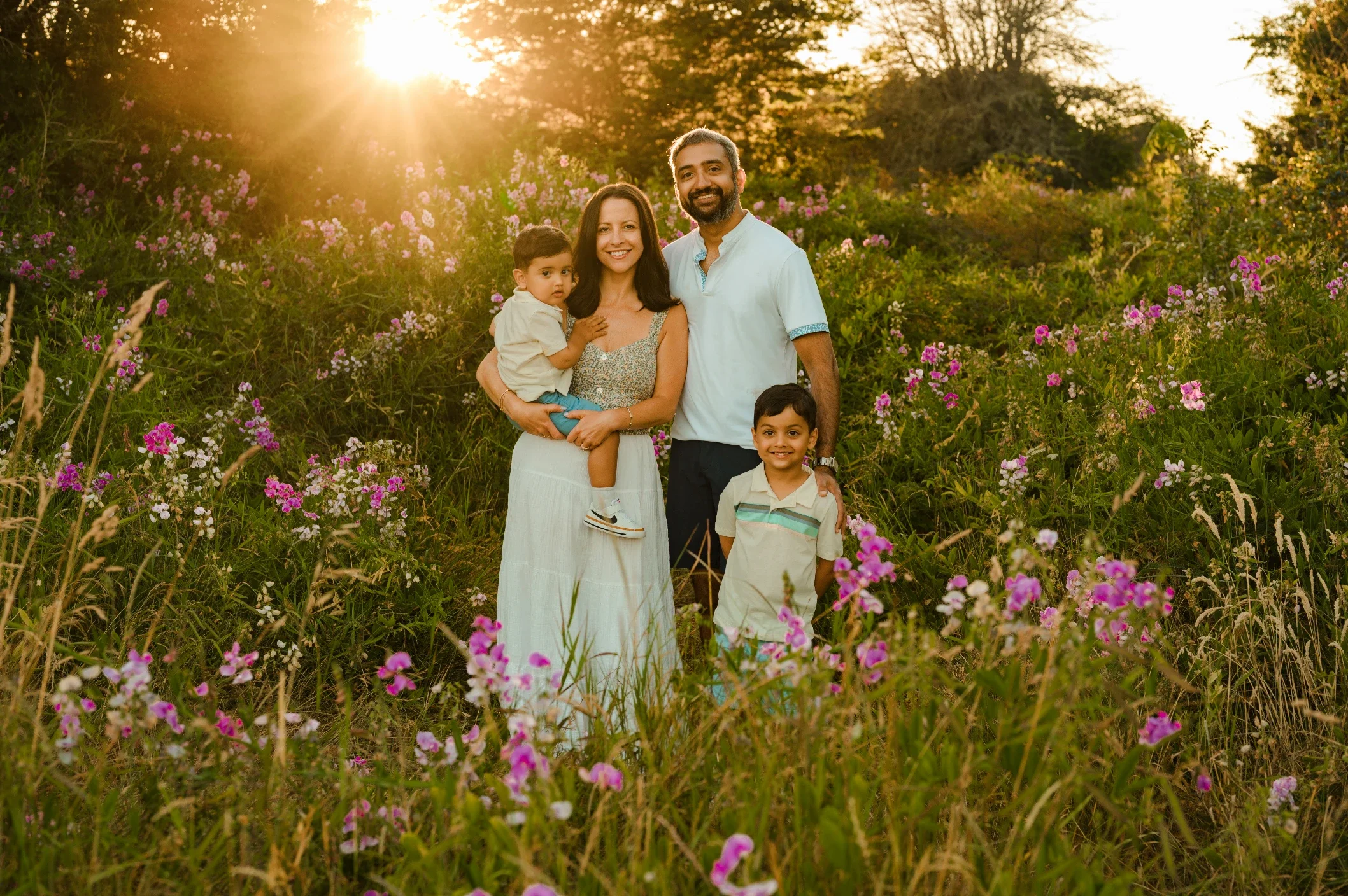 mom, dad, with two sons backlit by sunshine in a field of purple wilflowers, tall grass, and greenery