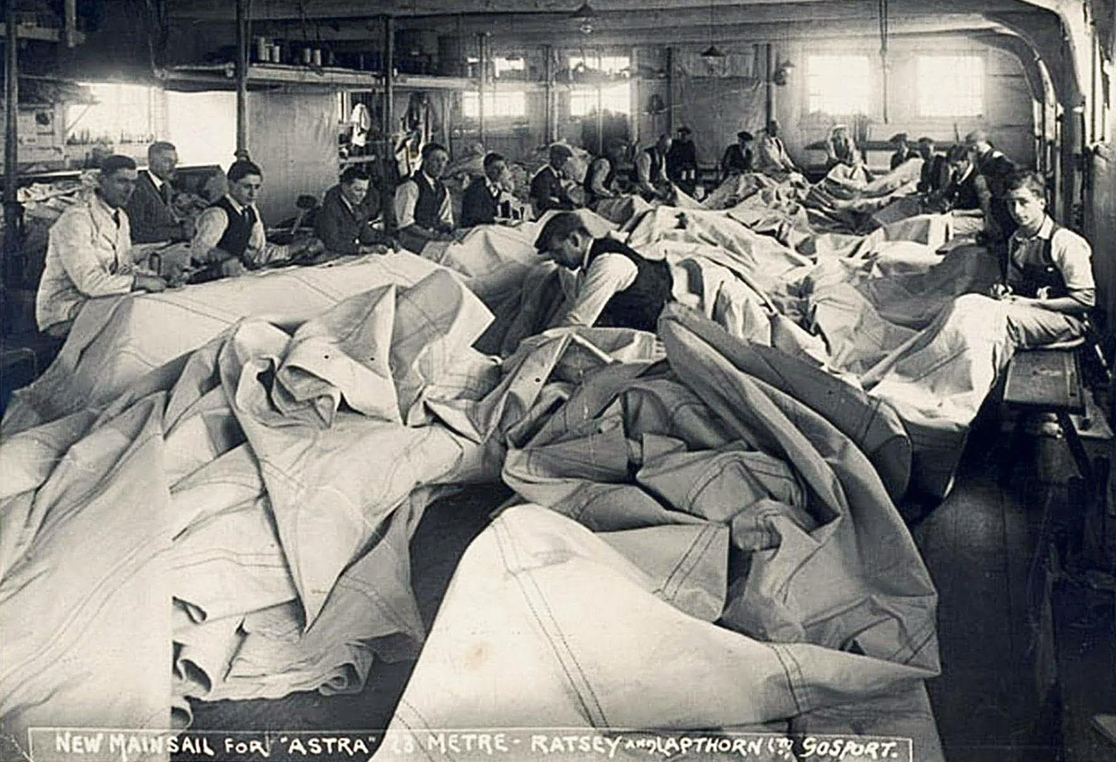 Black and white family photo of Ratsey family workers sewing fabric in a factory, with fabric pieces on desks and workers focused on their work.
