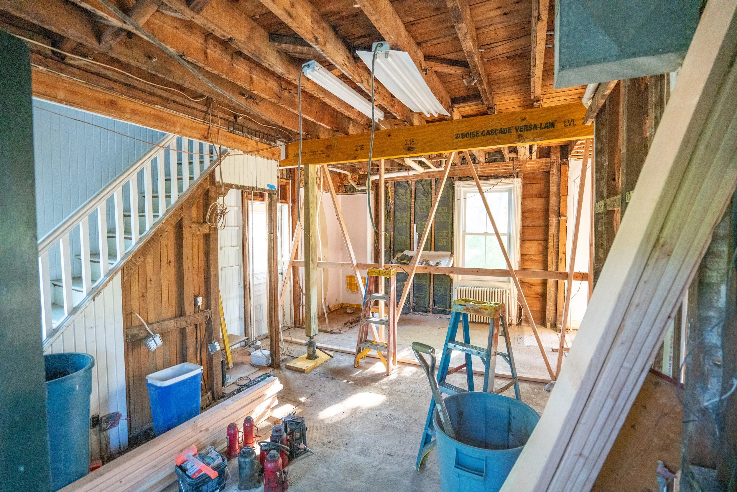 Interior of a house under renovation with exposed wooden beams, ladders, construction tools, and materials.