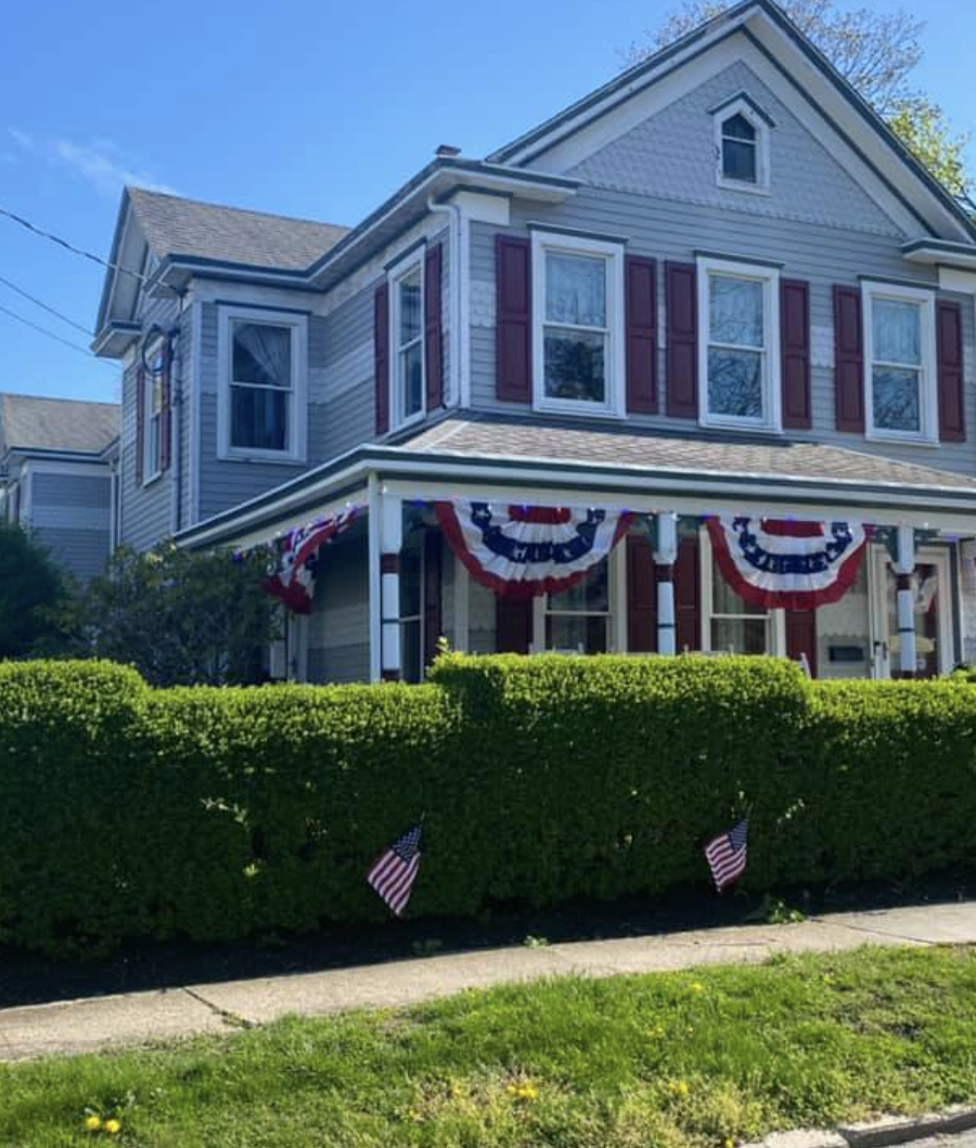A two-story house decorated with red, white, and blue patriotic bunting and small American flags, likely for a national holiday celebration.