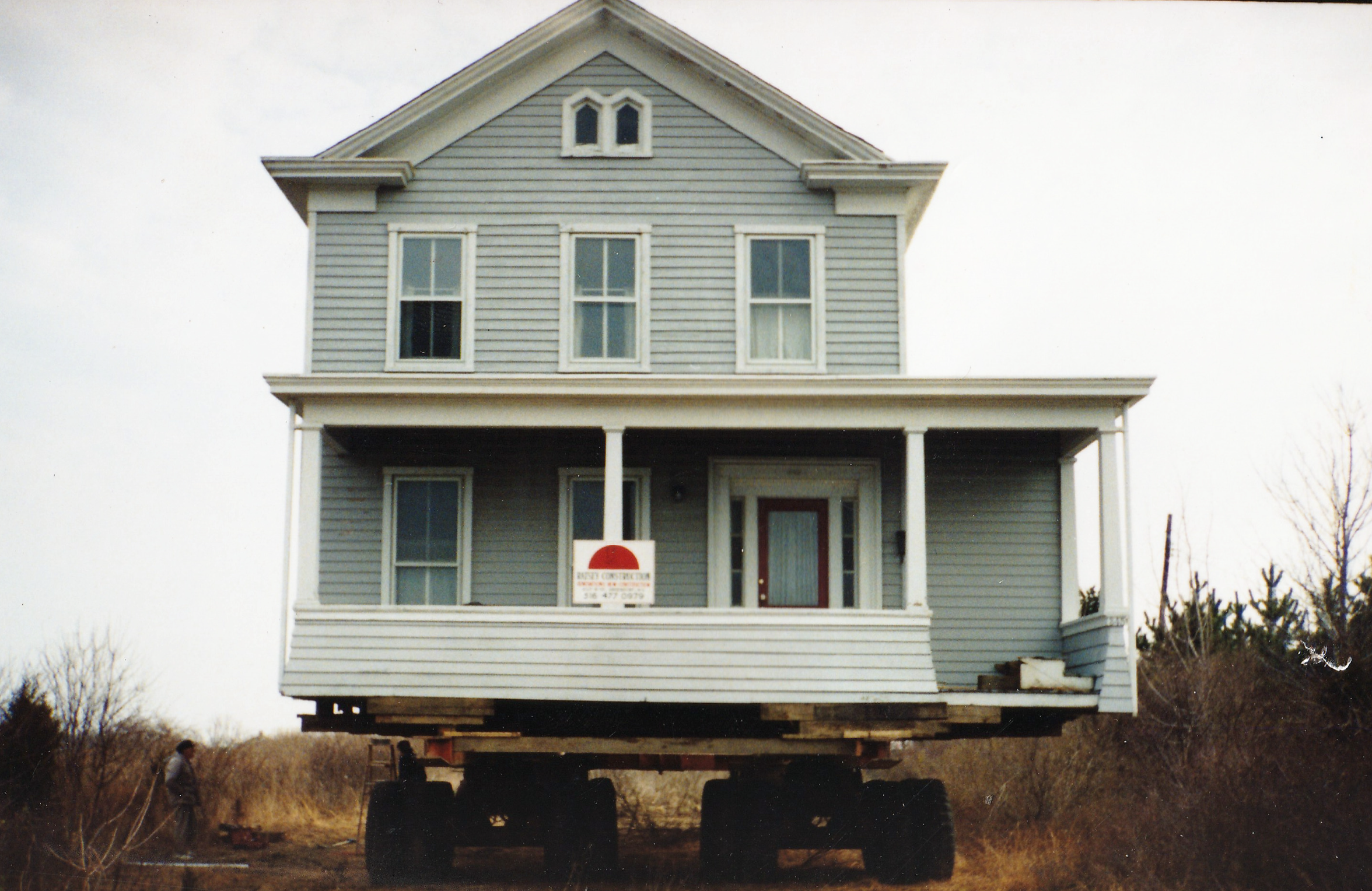 A large house on a flatbed trailer in an outdoor area, with construction or renovation in progress.