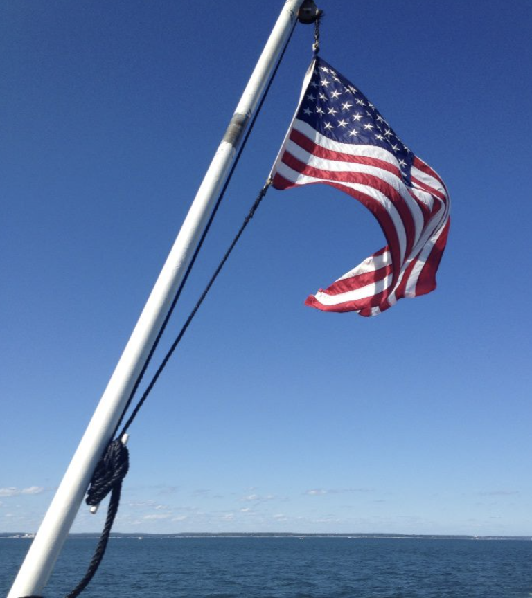 American flag flying on a flagpole over a body of water on a clear day.