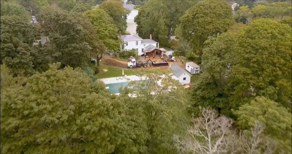 Aerial view of a backyard with a swimming pool, some trees, and a house. The yard is construction or renovation with equipment and debris.