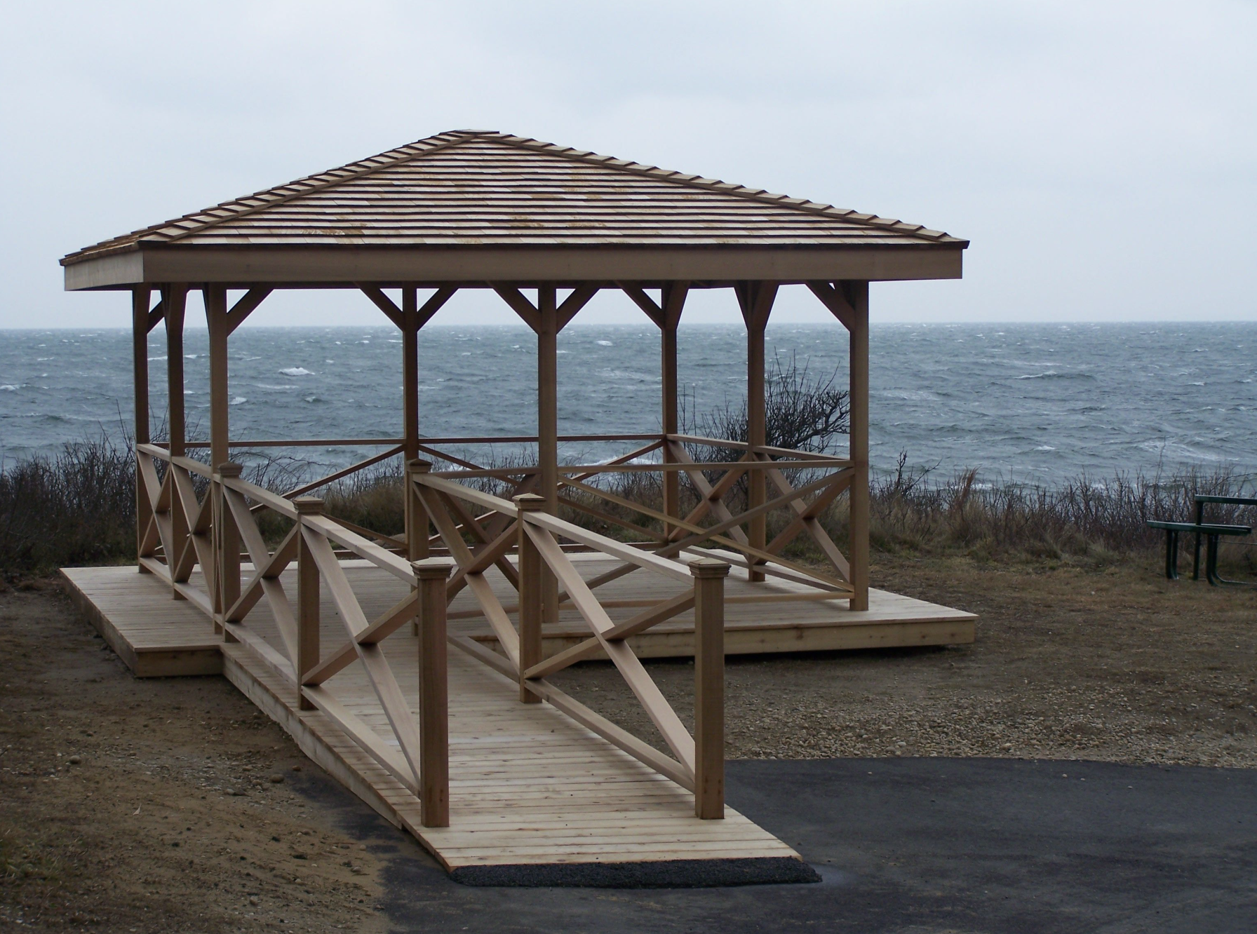 Wooden gazebo with a ramp overlooking a choppy ocean on a cloudy day.