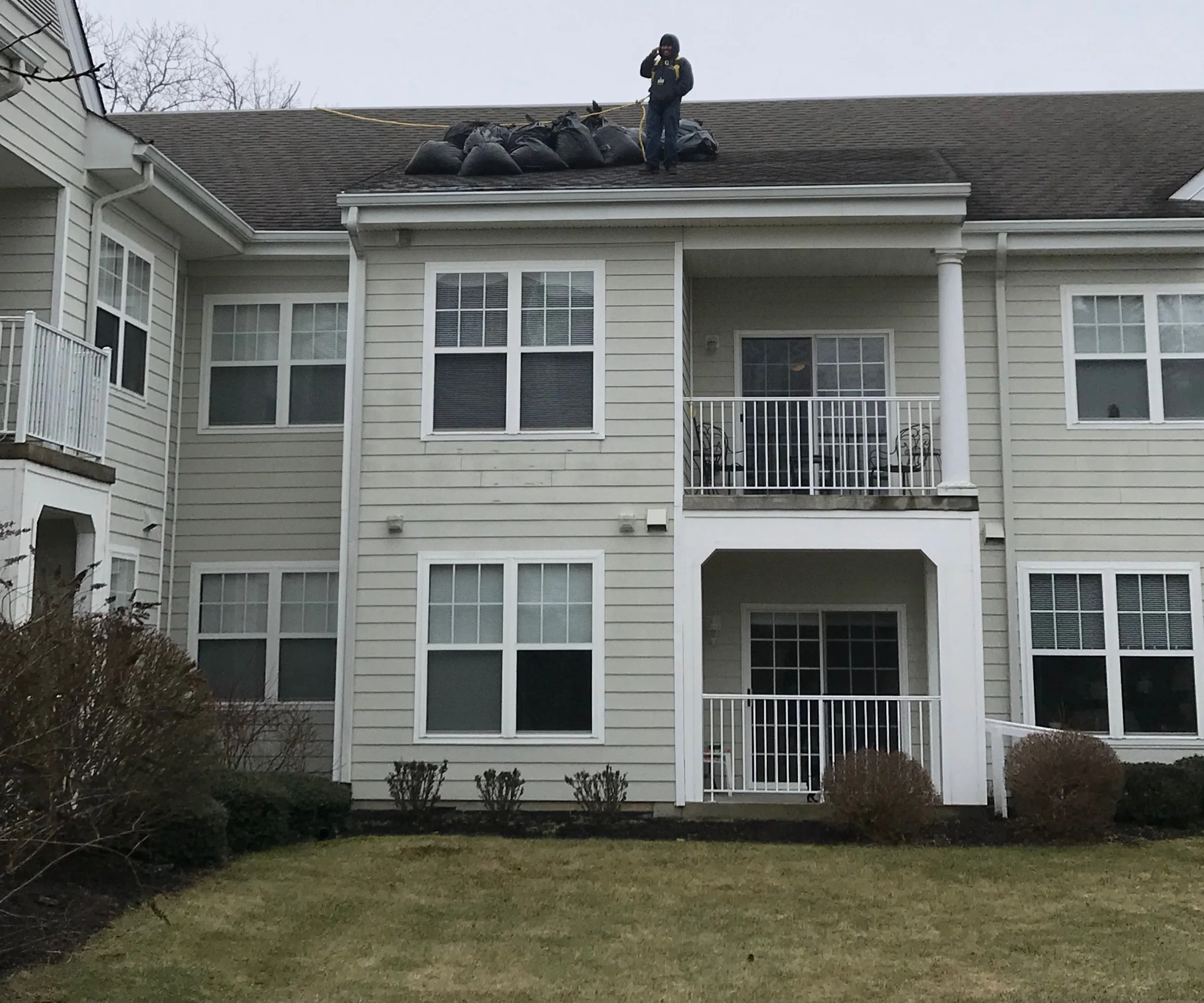 A person standing on the roof of an apartment building, surrounded by bags, possibly for roofing or maintenance work.