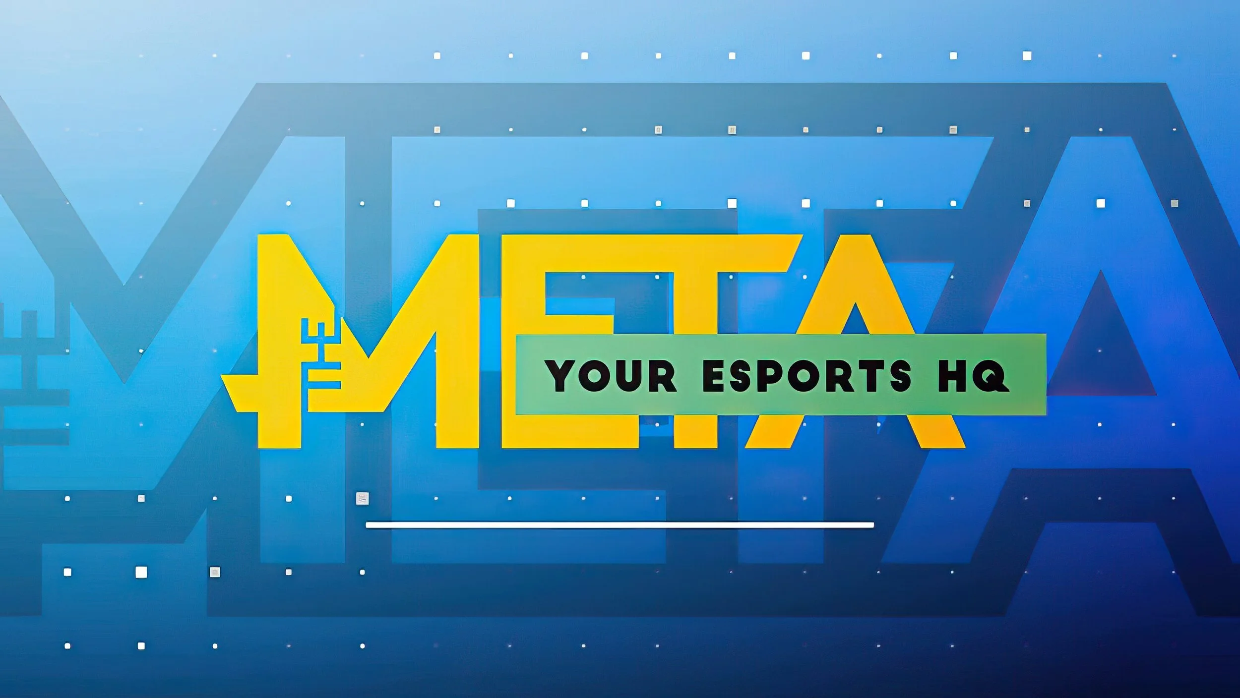 Sign reading 'META' in large yellow letters with green banner underneath that says 'YOUR ESPORTS HQ' on a blue patterned background.